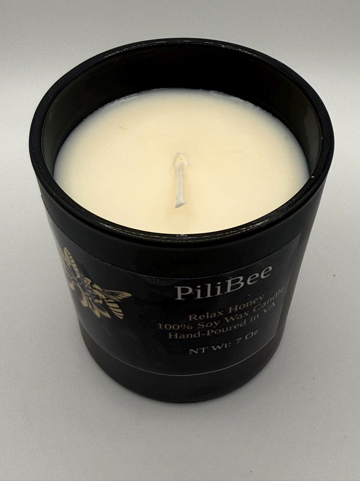 Black candle jar with a white candle inside, labeled 'PiliBee', on a gray background.