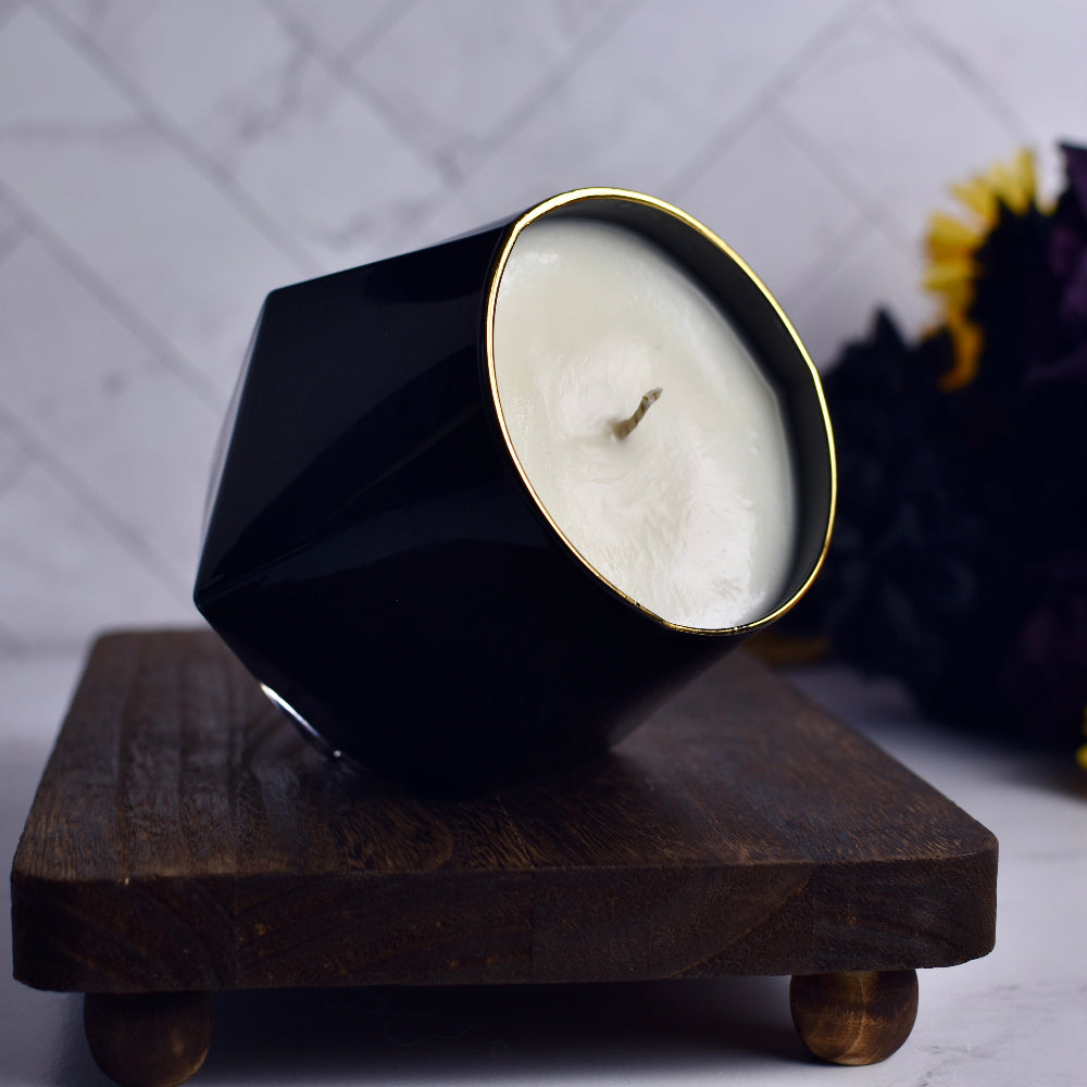 Black geometric candle holder with a white candle on a wooden stand against a blurred background