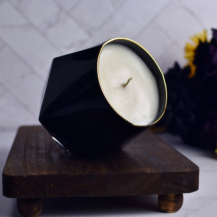 Black geometric candle holder with a white candle on a wooden stand against a blurred background