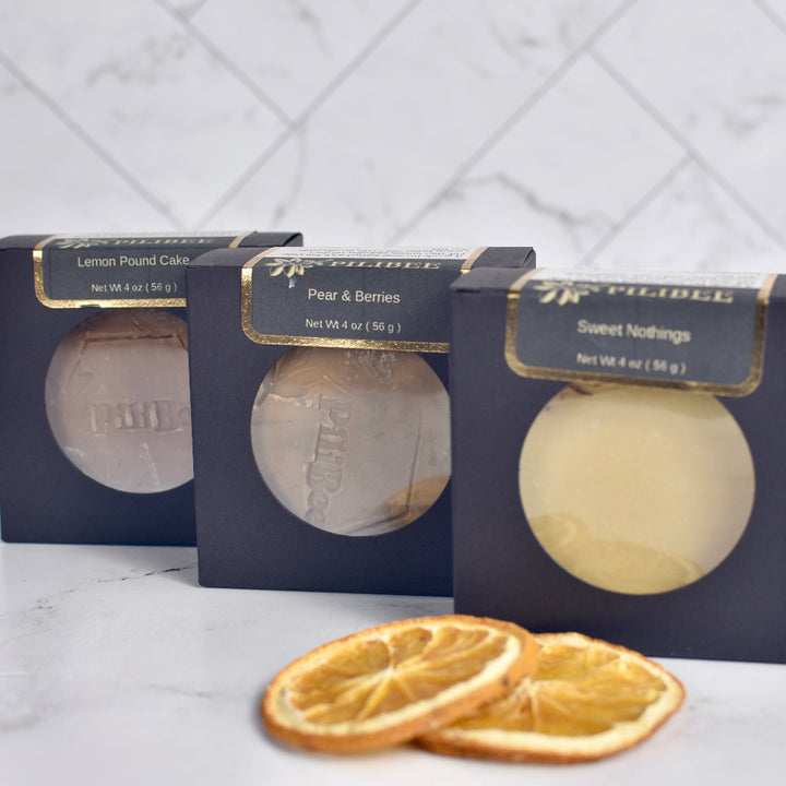 Three bar soaps in packaging with dried orange slices on a marble surface.