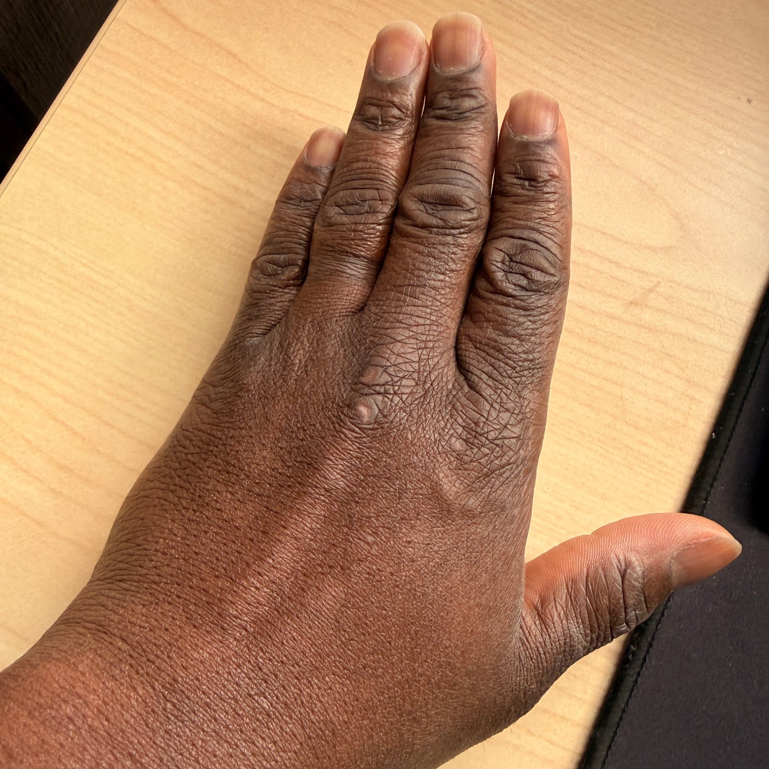 Close-up of a dark-skinned hand on a wooden surface