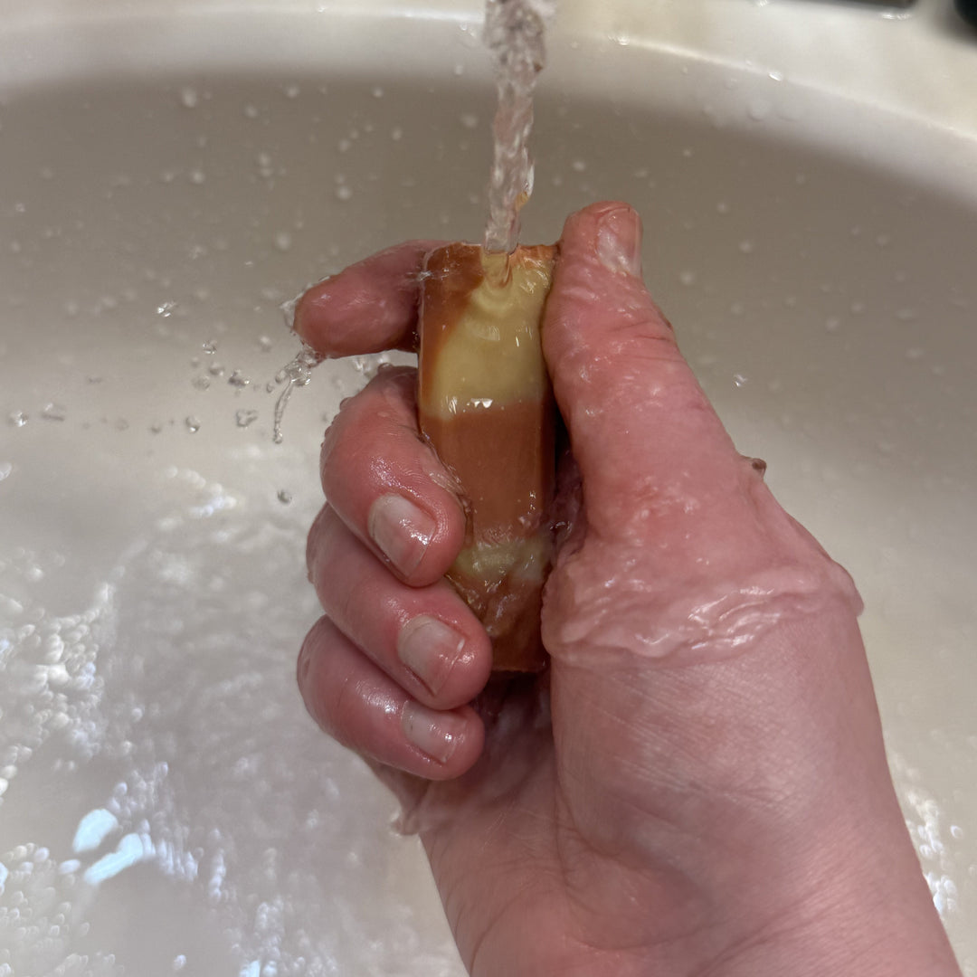 Hand washing a piece of fruit under running water in a sink.