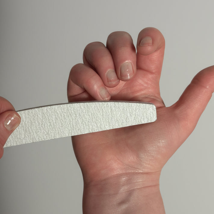 Person holding a white nail file against a neutral background