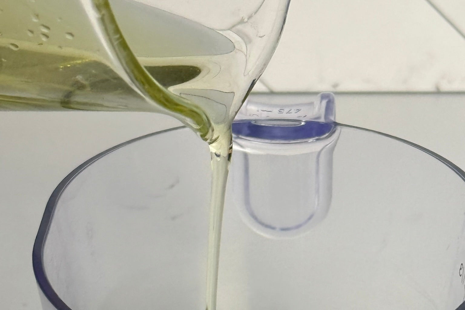 Oil being poured from a bottle into a clear measuring cup on a white background