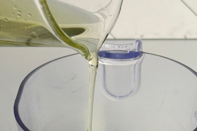 Oil being poured from a bottle into a clear measuring cup on a white background