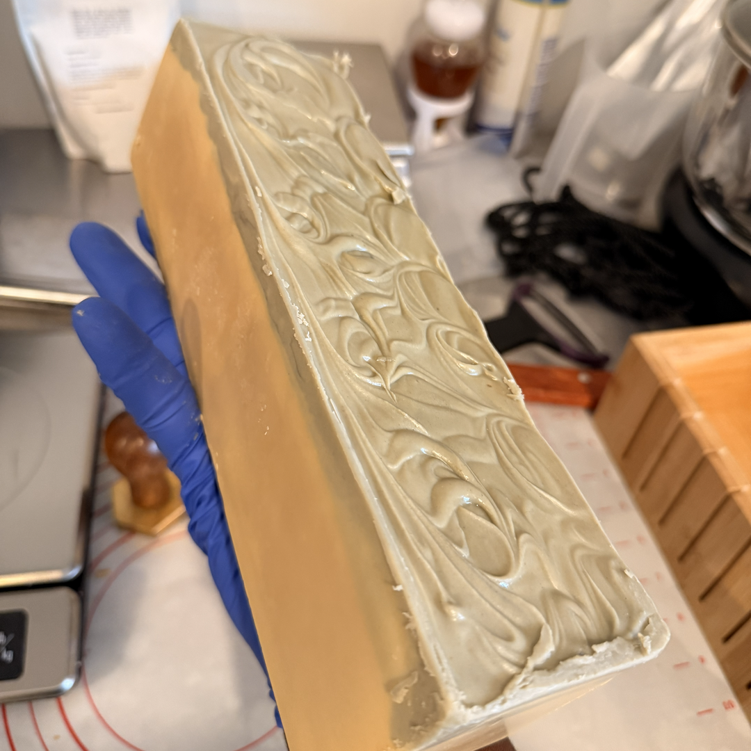 Bar of soap with decorative pattern held by a gloved hand in a kitchen setting